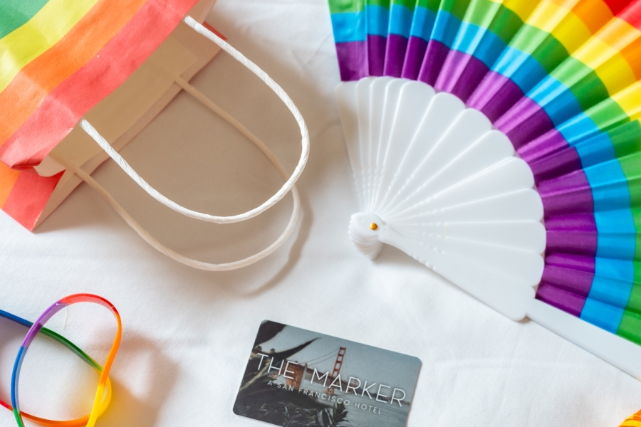 marker hotel key card on a bed with gay pride goodies: fan, lei, wristbands, and a bandana